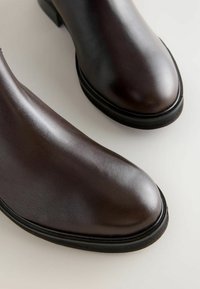 Bottes chevilles en cuir marron avec une texture lisse, bout rond et talon en caoutchouc bas. Présente une semelle de contraste noire.