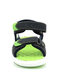 Sandalia infantil negra y verde con dos correas de velcro ajustables, plantilla texturizada y suela blanca. Nombre de la marca "Kickers" grabado en la correa.