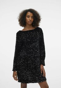 Musta sädelev kleit pika varrukaga, ümmarguse kaelusega ja lõtva istuvusega, millel on tekstuurne pind, kus sädelevad sequins peegeldavad valgust.