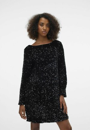 Musta sädelev kleit pika varrukaga, ümmarguse kaelusega ja lõtva istuvusega, millel on tekstuurne pind, kus sädelevad sequins peegeldavad valgust.