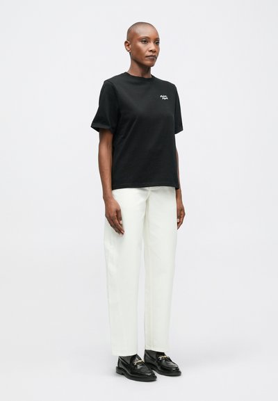 Černé bavlněné tričko s krátkým rukávem zdobené malým bílým logem, spárované s bílými rovnými kalhotami a černými mokasíny se zlatými detaily.