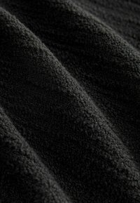 Zwarte, gestructureerde stof die een zachte, pluche oppervlakte toont met subtiele horizontale rimpels en diepte, geschikt voor meubelbekleding of kleding.