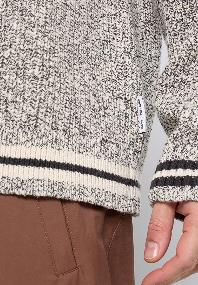Gestrickter Pullover in Grau und Creme, mit einem strukturierten Muster und dunklen Streifen am Saum und an den Bündchen. Etikett an der Seite sichtbar.