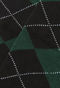 Svart och grön argyle-mönstrad tyg med vit sömnad. Mjuk textur, diamantformer framträdande. Slät och jämn väv.