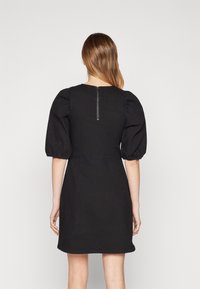 Czarna sukienka z krótkimi bufkami, dopasowanym fasonem i zapięciem na zamek z tyłu. Wykonana z gładkiego materiału o minimalistycznym wzorze.