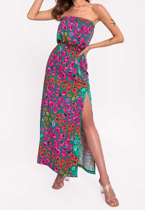 Femme portant une robe maxi verte sans bretelles avec des motifs de lèvres en rose, rouge et orange et motif léopard, dotée d'une fente latérale haute sur la cuisse et de talons transparents.