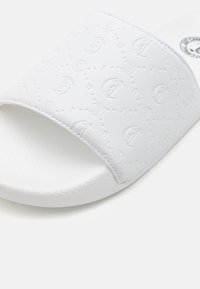 Hvide slide-sandaler med et præget logomønster på et glat materiale, med en tekstureret fodseng og rund sål.
