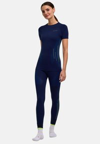 Completo sportivo blu navy con top a maniche corte e leggings aderenti. Presenta linee verdi a contrasto e dettagli testurizzati sulle gambe. Materiale liscio.