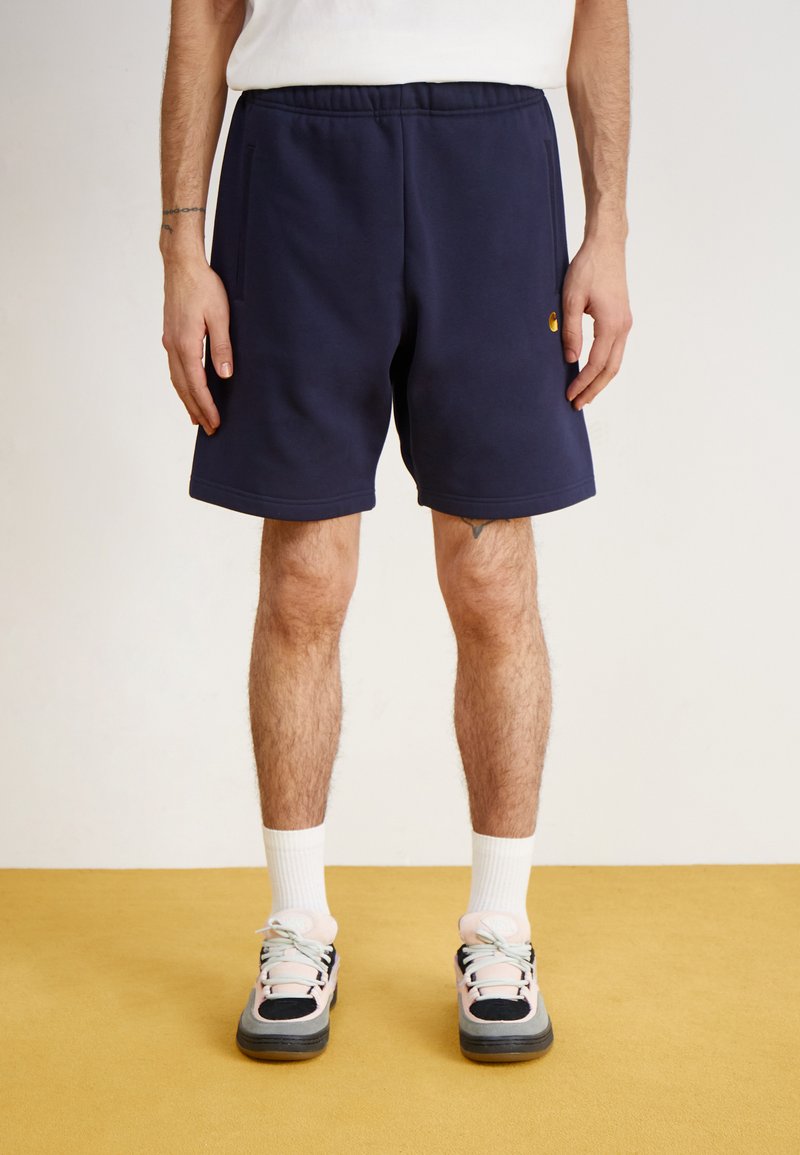Shorts bleu marine en tissu doux, avec une taille élastique et deux poches latérales. Portés avec des chaussettes blanches et des baskets multicolores.