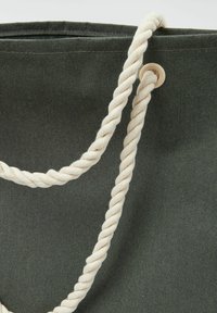 Zelená plátěná taška s krémovými zkroucenými rope držadly a očkem pro připevnění. Texturovaný povrch s vyztuženým švem podél okraje.