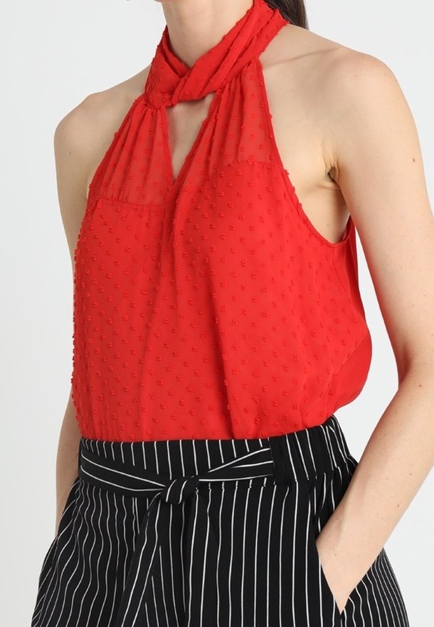 Haut rouge sans manches avec un col noué halter, présentant un motif à pois texturé. Accompagné d'un pantalon rayé noir et blanc avec une taille nouée.