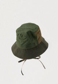 Πράσινο και καφέ καπέλο με φαρδύ γείσο και ρυθμιζόμενες λουρίδες από κάτω στον απλό ανοιχτό φόντο.