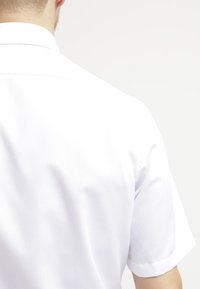 Lyhythihainen valkoinen paita, sileää kangasta, klassinen kaulus, puhdas muotoilu takanäkymässä, hienovarainen rakenne. Ei näkyviä kuvioita tai korostuksia.