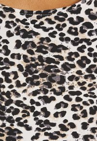 Leopardmönstrad tyg med svarta och mörkgrå fläckar på en vit bakgrund, med en subtil beige detalj. Slät, strukturerad yta.