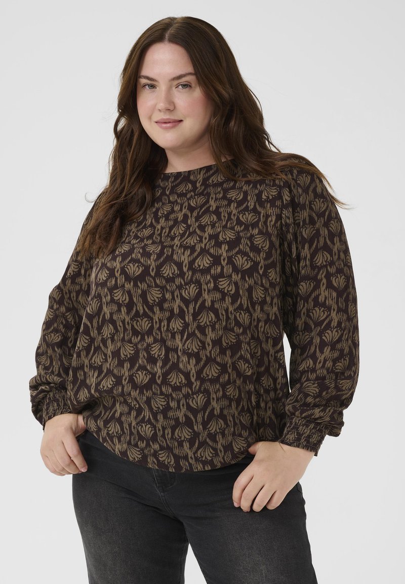 Schwarze Bluse mit einem beigen Blumenmuster, langärmlig und mit rundem Halsausschnitt. Der Stoff hat ein strukturiertes Aussehen.