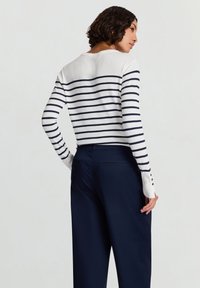 Maglione a righe blu navy e bianche con maniche lunghe, scollo rotondo e dettagli con bottoni sui polsini, abbinato a pantaloni blu navy.