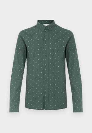 Camisa verde de manga larga con cuello abotonado, que presenta un sutil patrón de pequeños diamantes azul claro y un dobladillo recto.