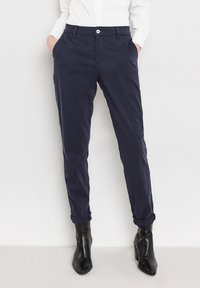 Navy chinos with a tailored fit, featuring side pockets, a button closure, and rolled cuffs, paired with black ankle boots.