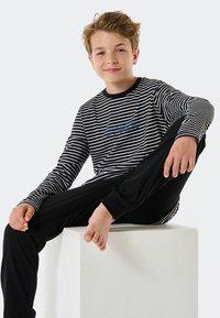 Camisa de manga larga a rayas en blanco y negro con el texto "break", combinada con pantalones negros. Diseño simple y casual; tejido suave, corte relajado.
