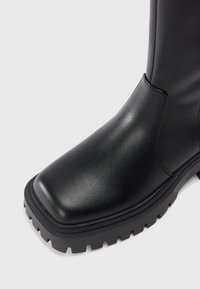 Čierne kožené členkové topánky so štvorcovou špičkou, textúrovaným povrchom a robuste čierne gumové podrážky s hlbokým dezénom pre lepšie priľnutie.