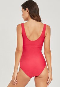 Rode badpak met brede banden, een ronde rug, een soepele textuur en een getailleerd ontwerp. Geen zichtbare patronen of hardwaredetails.