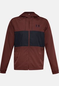 Chaqueta cortavientos con capucha en color burdeos, con un panel azul marino en el pecho. Cuenta con una cremallera frontal y puños elásticos.