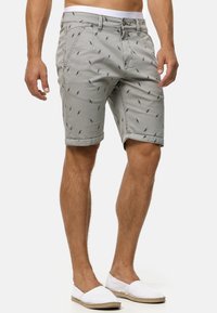 Shorts gris clair avec de petits motifs d'oiseaux bleus, fabriqués en coton. Présentent une coupe classique, des ourlets roulés et une fermeture éclair avec un bouton.