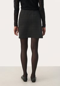 Grau karierten Minirock mit einer taillierten Passform, kombiniert mit schwarzen, transparenten Strumpfhosen und schwarzen flachen Schuhen. Sichtbares Muster aus Spitze mit langen Ärmel.