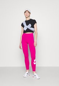 Leggings rosa con logo, maglietta nera corta, pullover grigio e scarpe da ginnastica bianche con accenni grigi e rossi. Design semplice e moderno.