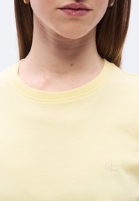 Ανοιχτό κίτρινο βαμβακερό t-shirt με στρογγυλή λαιμόκοψη και μικρό λευκό κεντητό λογότυπο στο αριστερό μέρος του στήθους. Μαλακή υφή με μίνιμαλ σχεδιασμό.