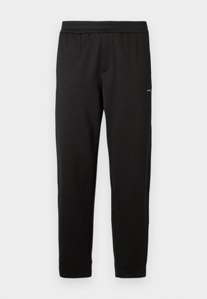 Calças de sweatpants pretas com cintura elástica, pernas ajustadas e um pequeno logótipo na parte superior da coxa, exibidas sobre um fundo branco.