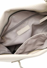 White leather handbag interior featuring a beige lining, a zippered pocket, and a label. Notable quilted texture and gold hardware accents.