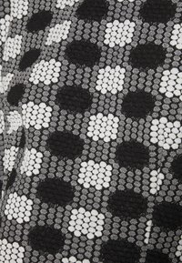Tecido texturizado com um padrão quadriculado em preto e branco, apresentando tamanhos de pontos variados, criando um contraste tátil no design.