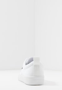 Białe płócienne trampki z płaską podeszwą, wyściełanym kołnierzem i uchwytem z tyłu. Posiadają subtelne przeszycia i minimalistyczny design.