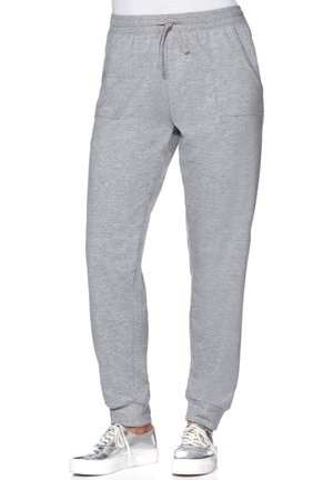 Pantalon de survêtement gris clair avec taille à cordon et poches avant, porté avec des baskets argentées à lacets sur une personne debout.
