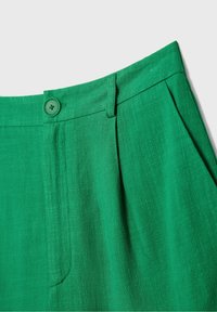 Pantalon en tissu vert avec fermeture à bouton, passants de ceinture, plis sur le devant et poches latérales, présenté sur un fond uni.