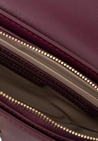Borsa strutturata bordeaux con numerosi scomparti con zip, fodera interna liscia e rifiniture in metallo dorato.