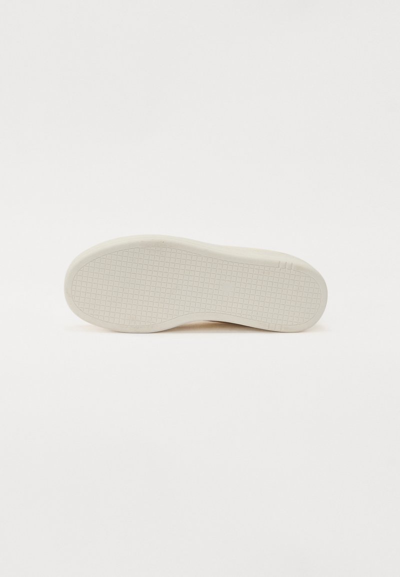 Semelle de chaussure en caoutchouc blanc cassé, texturée avec de petits carrés et des lignes pour l'adhérence, présentant des bords arrondis et un profil légèrement surélevé.
