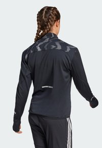 Black athletic jacket with a textured camo pattern on the shoulders, long sleeves, and reflective accents at the cuffs and back.