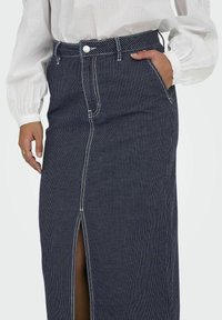 Gonna maxi in denim con strisce bianche verticali, spacco frontale e classico design a cinque tasche. Rifinita con cuciture bianche a contrasto.