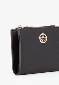 Portafoglio in pelle nera con superficie strutturata, caratterizzato da un emblema circolare dorato e chiusura con zip. Design compatto con bordi arrotondati.