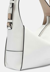Biała skórzana torba na ramię o trójkątnym kształcie, z czarnymi akcentami i zapięciem na zamek. Posiada odpinany pasek oraz widoczne detale szwów.