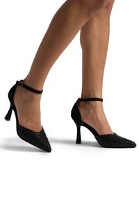 Scarpe nere con tacco alto, punta affusolata, texture lucida di paillettes nella parte anteriore e dettaglio con cinturino alla caviglia. Design del tacco leggermente curvato.