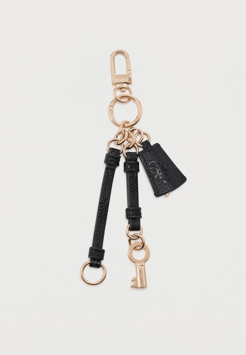 Μπρελόκ σε χρυσή απόχρωση με μαύρα λουριά από δέρμα με υφή, ένα μικρό γούρι σε σχήμα κλειδιού και μια τριγωνική ετικέτα από δέρμα με ανάγλυφο λογότυπο.