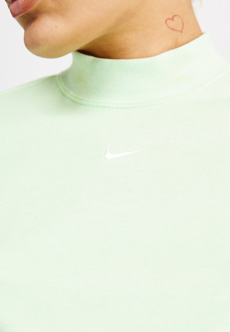 Top de manga larga verde menta con un cuello alto, que presenta un pequeño logo blanco de Nike en el pecho, confeccionado con tejido de punto suave.