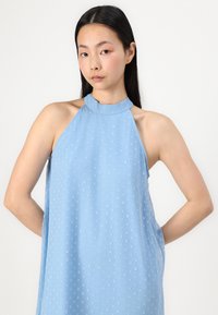 Light blue sleeveless dress with a high neck, featuring a subtle textured pattern of raised dots throughout the fabric.