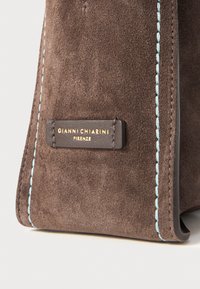 Brown suede bag with light blue stitching. Features a rectangular tag embossed with "GIANNI CHIARINI FIRENZE" in gold lettering.