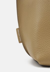 Brun läderväska med texturerad yta. Har en diskret logotypetikett och en böjd form som framhäver materialets mjukhet.