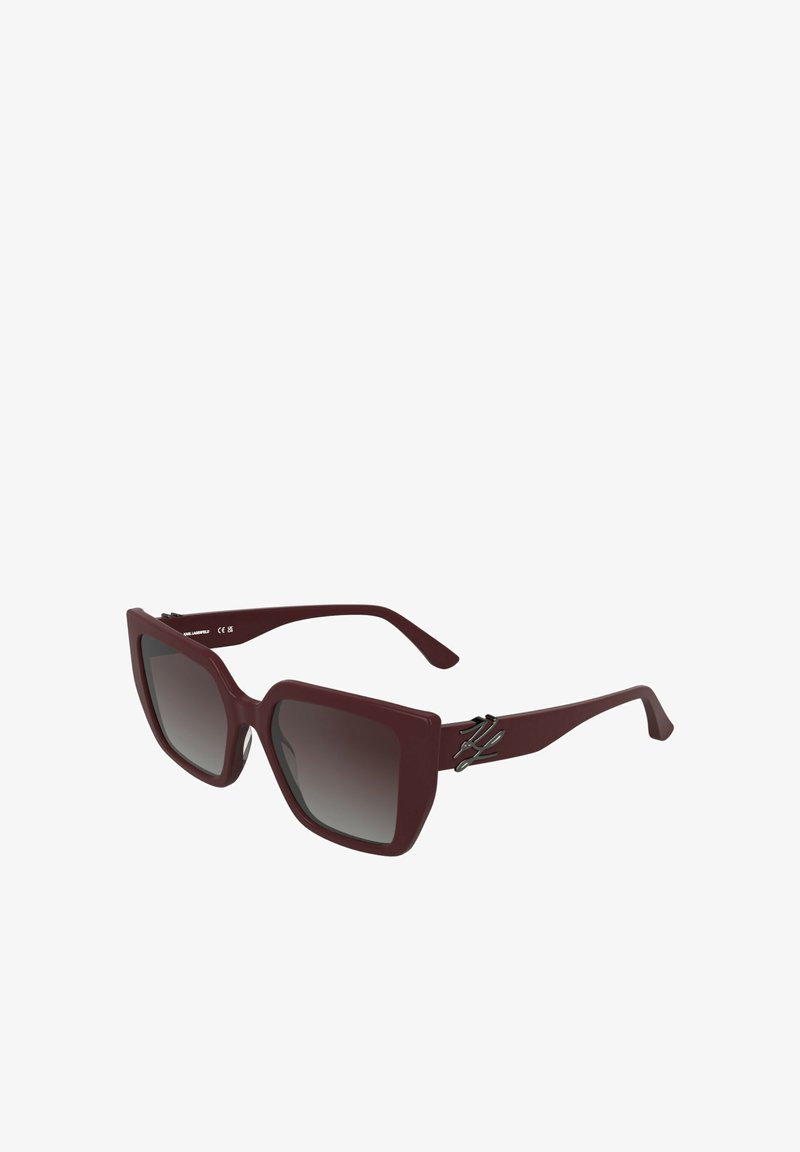 Lunettes de soleil oversize bordeaux avec verres dégradés, monture carrée audacieuse et accent métallique sur les branches.