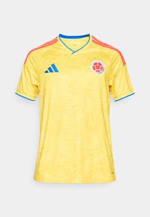 Camiseta de fútbol amarilla con rayas rojas en los hombros, ribete azul, patrón de mariposas, logo de Adidas y emblema de la selección nacional de Colombia en el pecho.